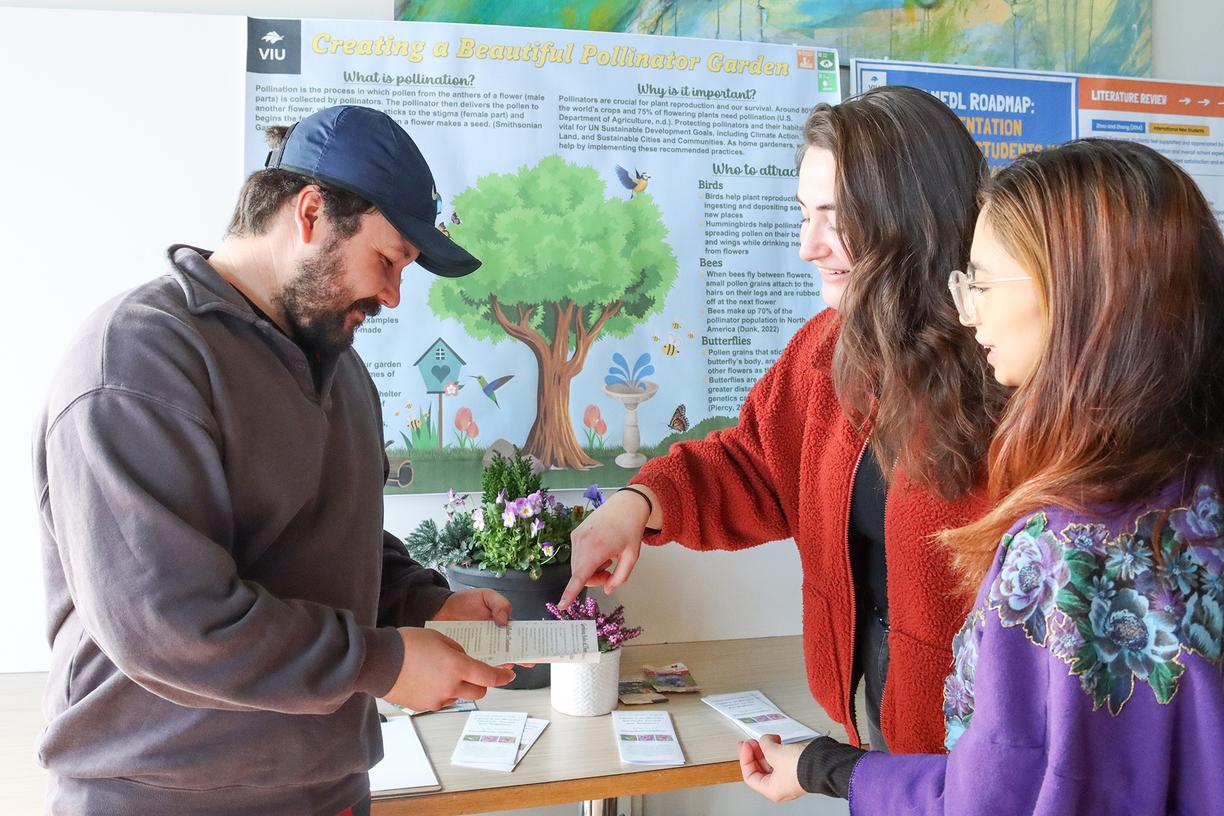 Three students look at a pamphlet in front of their CREATE research poster.