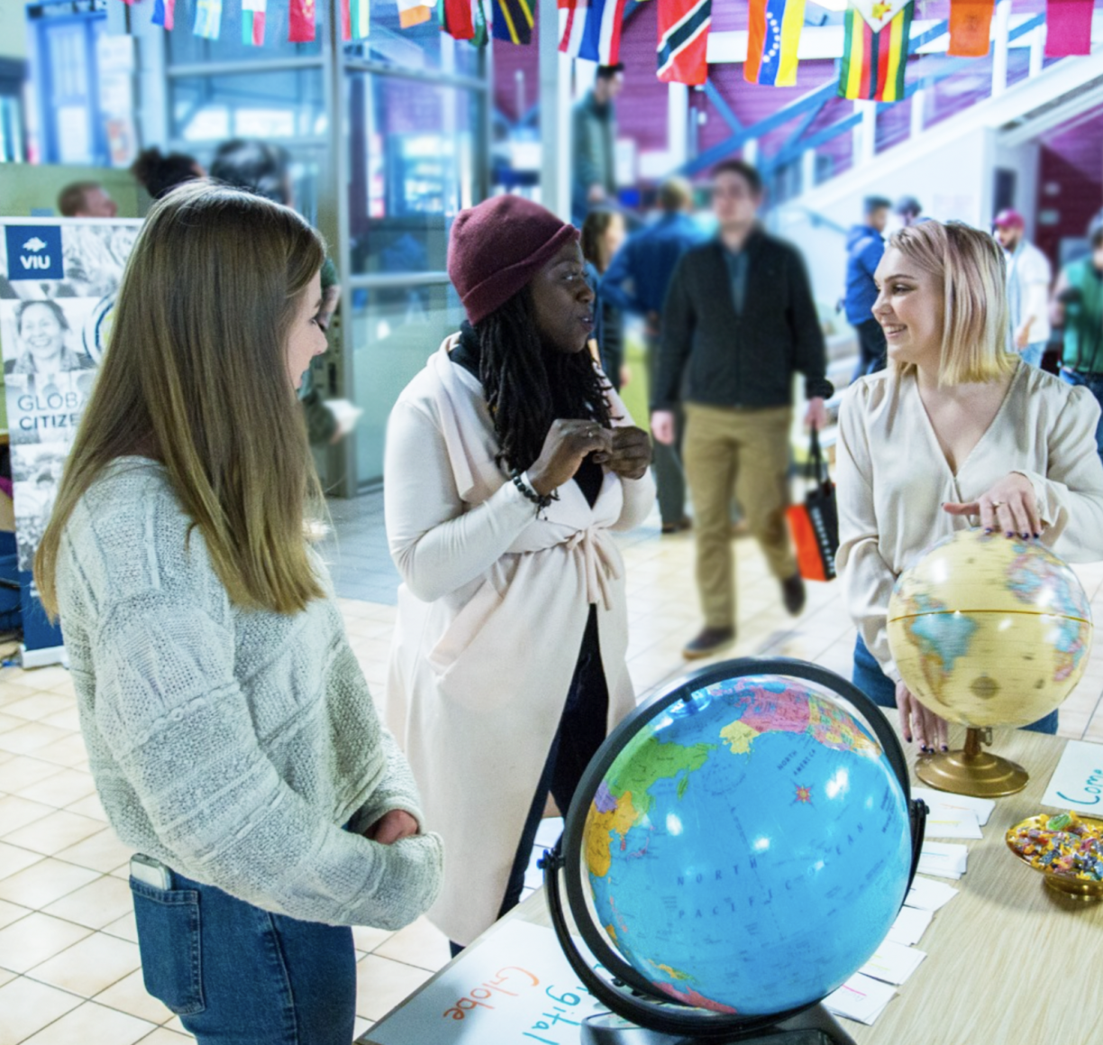 Three woman standing and chatting in front of a table on which sits two globes.