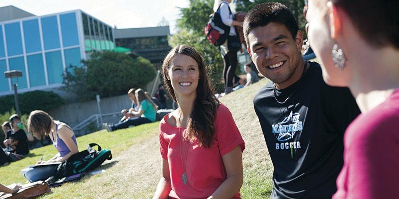 Three students chat while sitting on the lawn at VIU's Nanaimo campus.