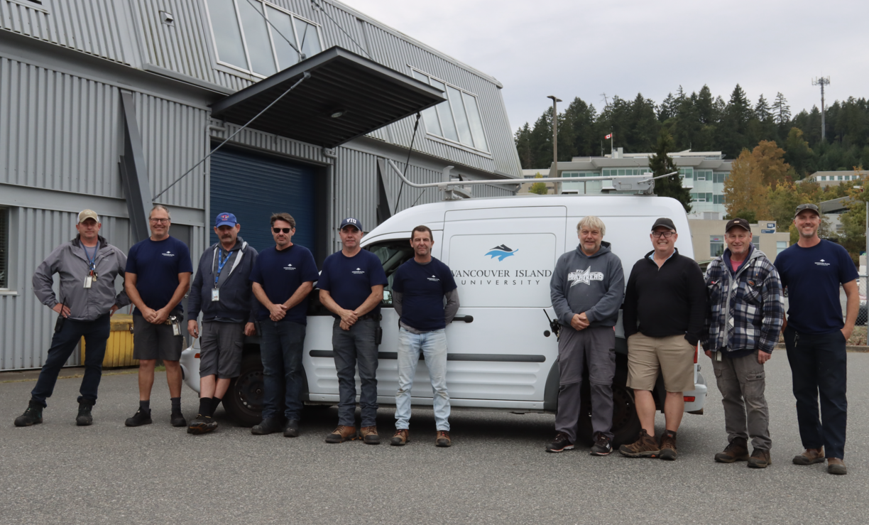 The facilities team at VIU standing outside in front of a work van on a cloudy day