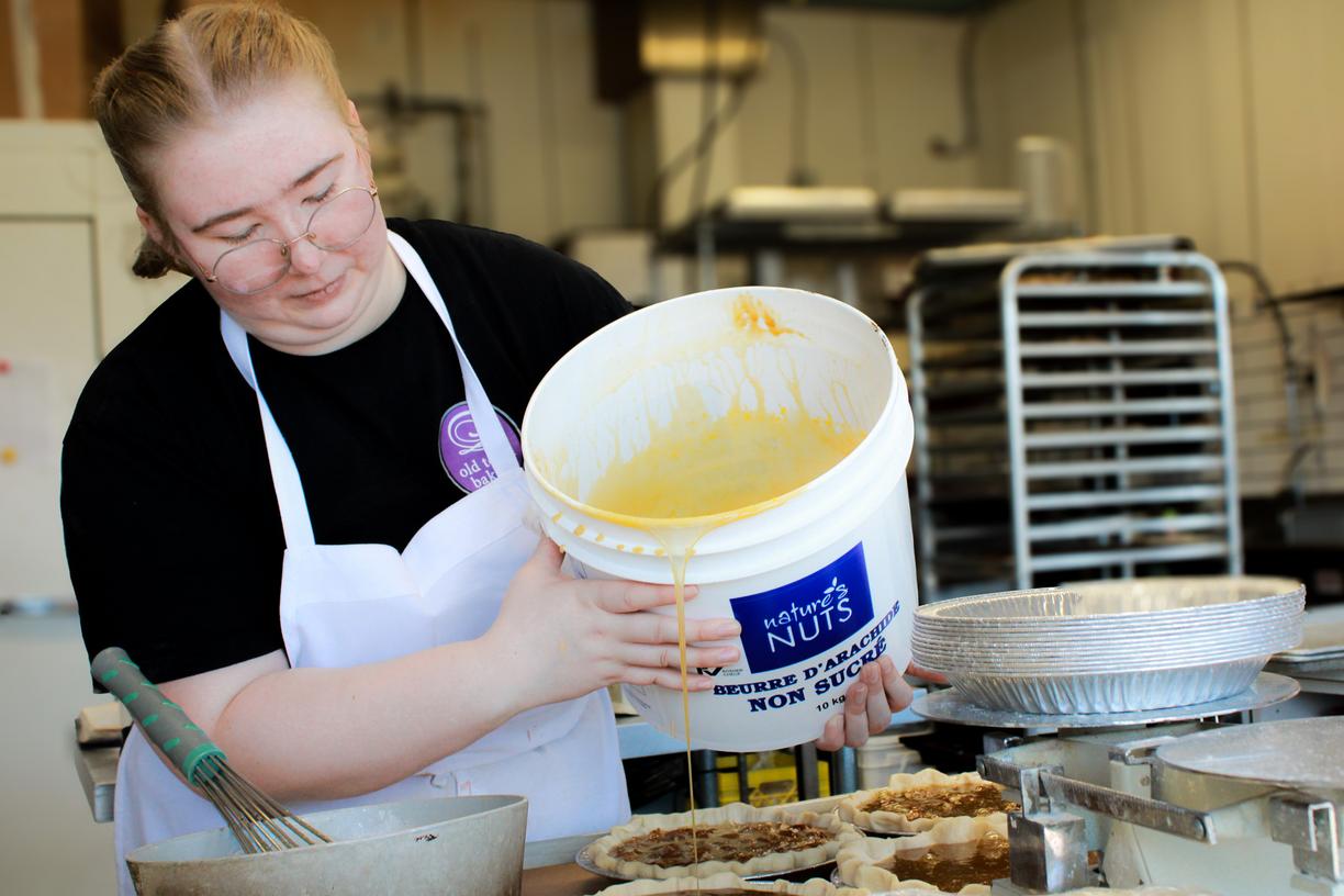 Faithe Haley, wearing a black shirt and white apron, pours sugar into pies in an industrial kitchen.