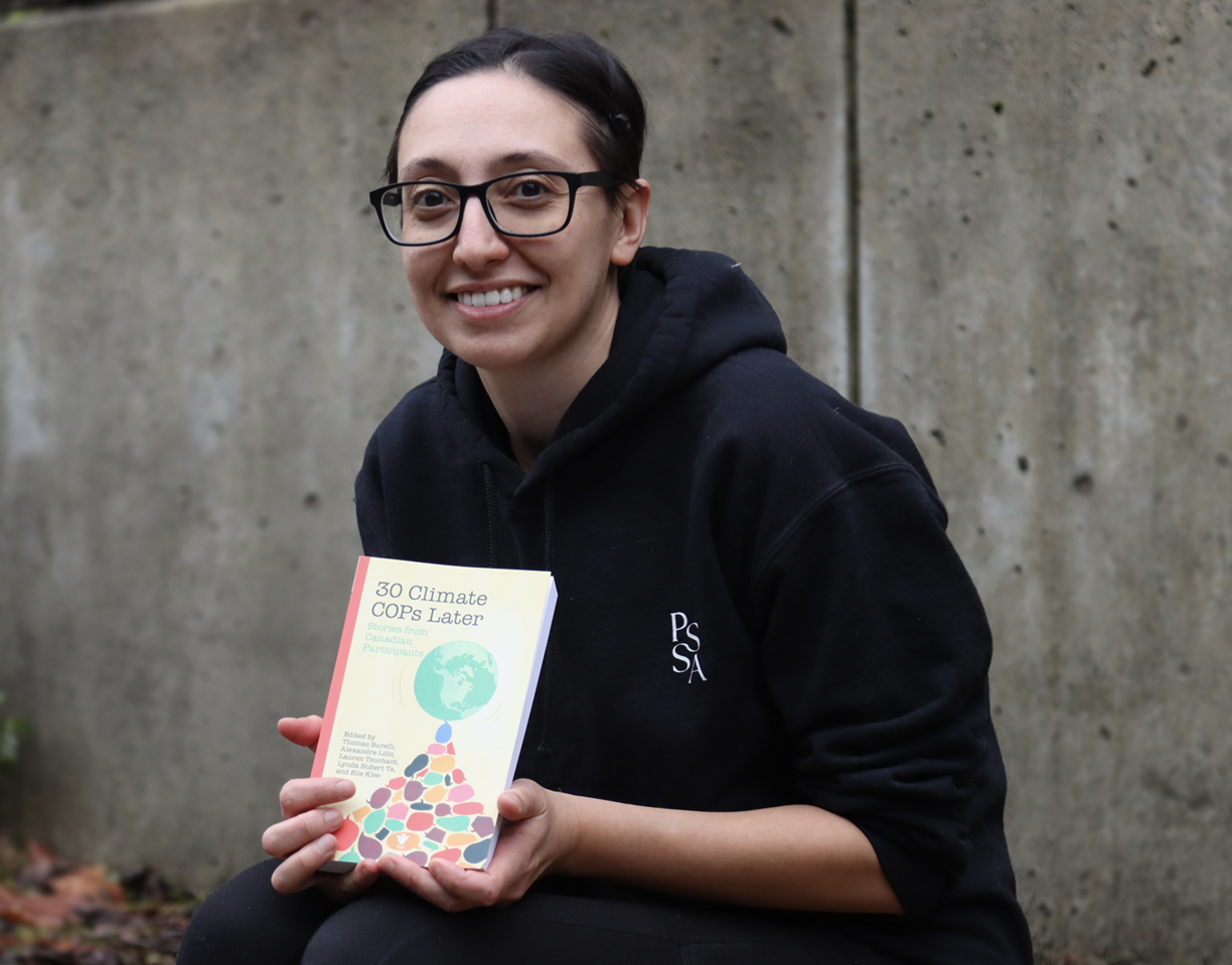 Lauren Touchant sitting outside and displaying her book and smiling at the camera.