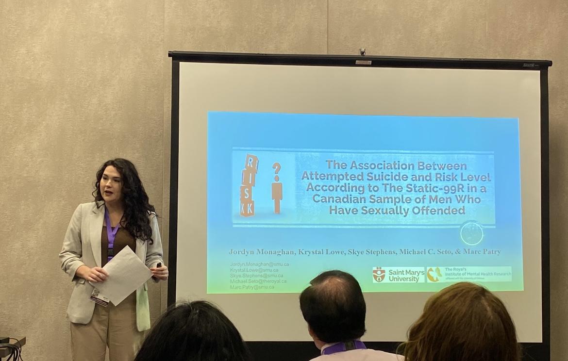 Jordyn speaks at a conference, standing next to a screen 