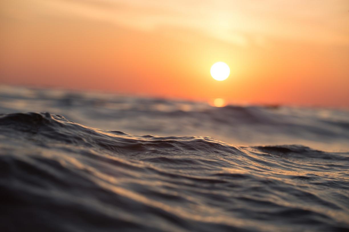 An orange and yellow sunset above ocean waves.