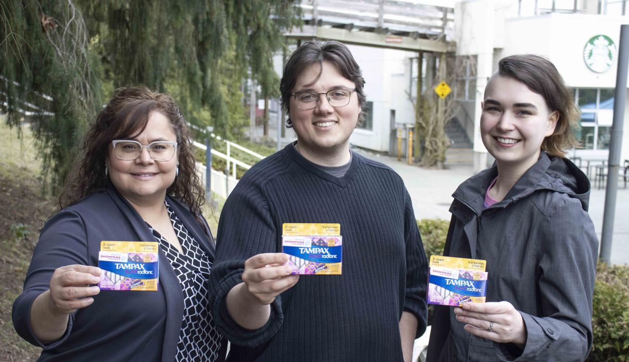 Three people hold up tampon boxes