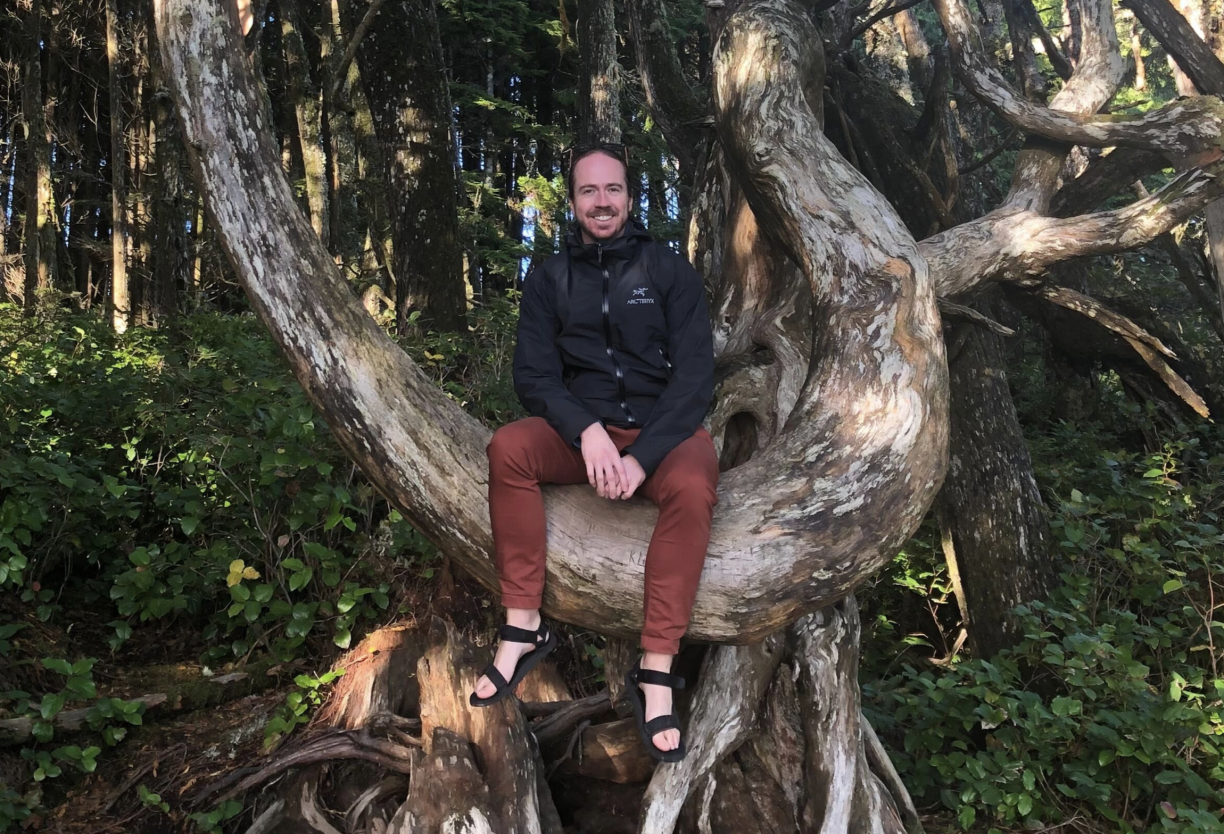 Dr. Michael Asmussen sitting in a tree and smiling at the camera.