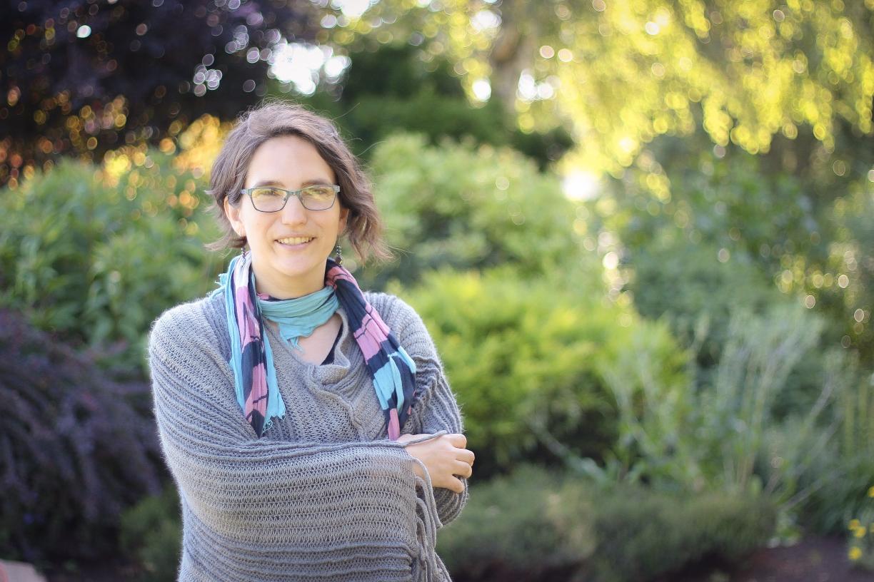 Sharon Karsten standing and smiling with her arms crossed in front of a blurred background of greenery