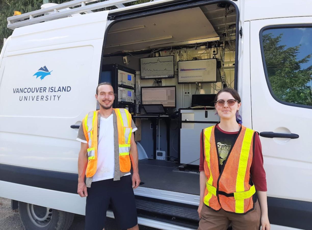 Trevor Michalchuk and Lily Eggert, wearing high visibility vests, while standing in front of the Mass Specmobile.