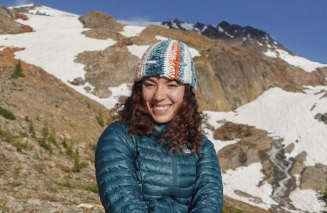 Amanda Hulsen sitting outside on a sunny day hike and smiling at the camera.