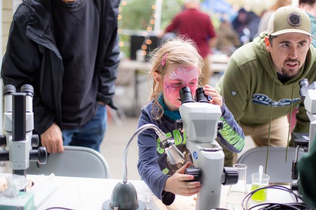 A young girl looking through a microscope during an exhibit at VIU Fest.