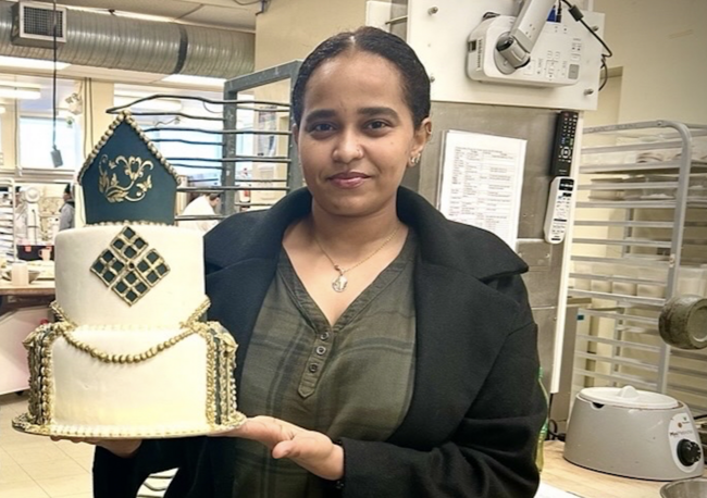Zuhur holding a cake she made and smiling at the camera.