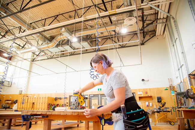 A female carpentry student cuts a board in the shop