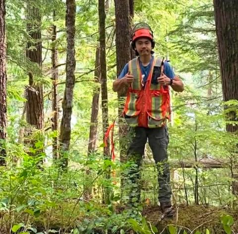 Kenji Boyko stands in the forest wearing a hard hat and reflective vest.