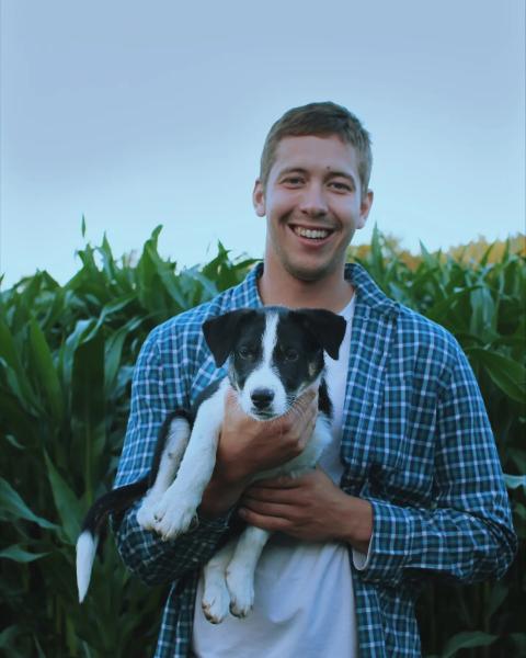 Douglas Groenendijk holds a black and white dog while standing in a field.