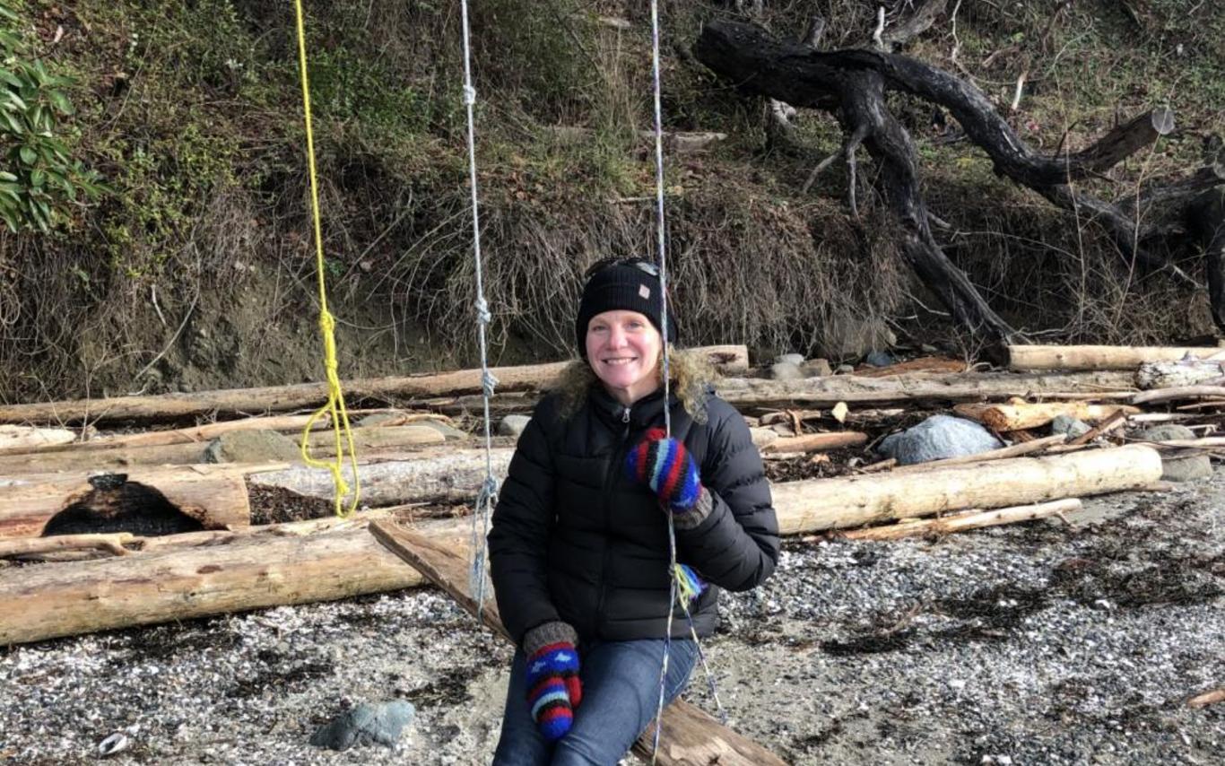 Christin Collishaw sitting outside in a swing at beach and smiling at the camera