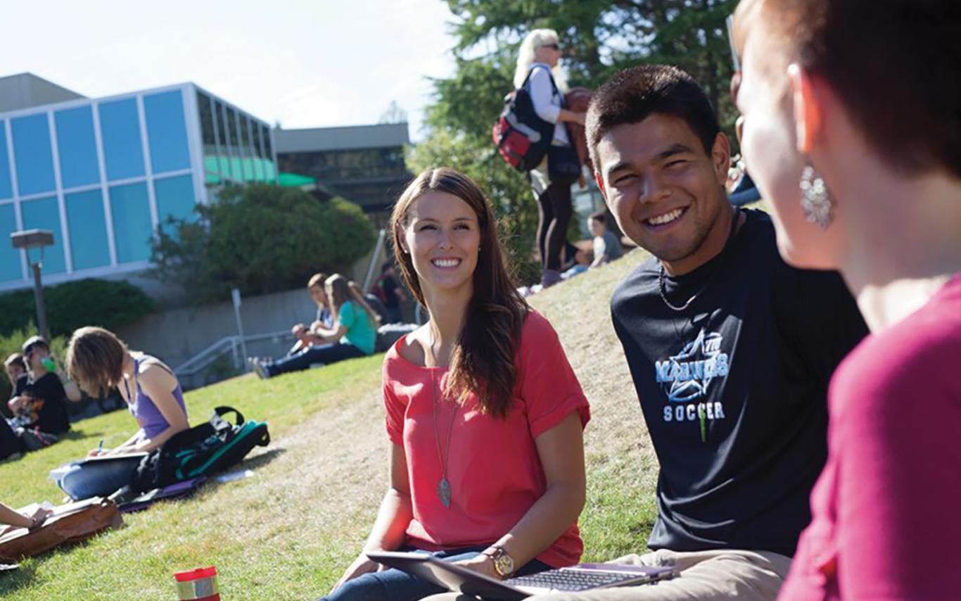 Three students sitting on lawn interacting with each other