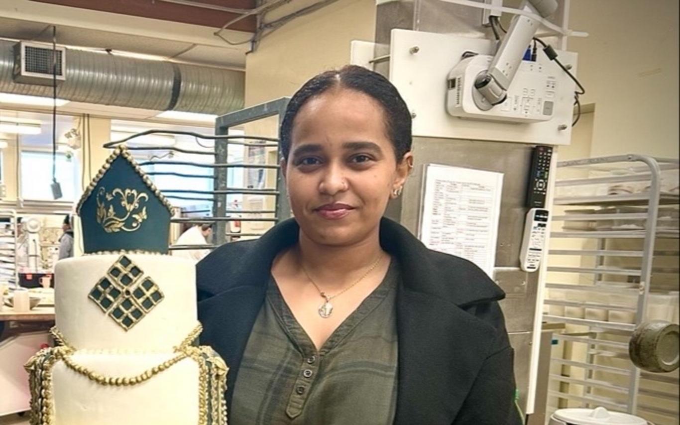 Zuhur Debasay holding a cake she made at VIU and smiling at the camera.